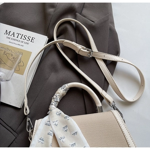 Detail of a beige woven handbag with silk scarf handle on a grey suit and art book