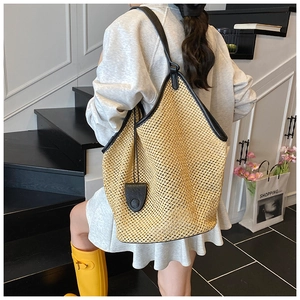 Detail of a woven straw tote with black leather trim and handles on a fashion model