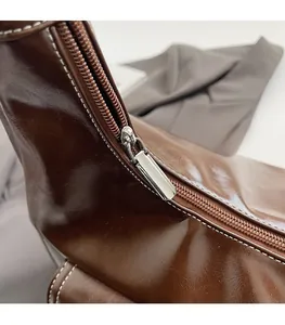 Close-up of smooth metal zipper and premium oil wax leather texture on brown shoulder bag