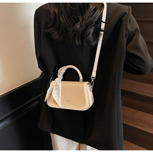 Detail view of cream crossbody bag with patterned scarf handle on a model in black blazer