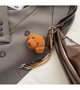 Close-up of curly brown plush poodle bag charm with woven strap on leather handbag