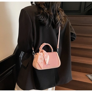 Detail of pink crossbody bag with heart print silk scarf handle decoration on black jacket