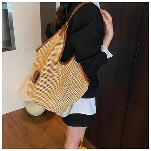 Detail of a large woven straw hobo bag with brown leather straps shown on a model