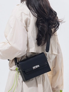 Classic black leather Kelly bag featuring a silver twist lock on a beige blazer background