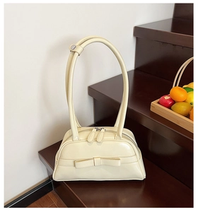 Detail of elegant cream bowling bag featuring dual top handles and stylish bow accent