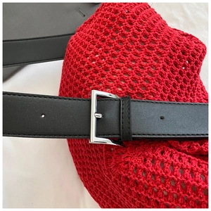 Close-up of black leather strap with silver buckle on red woven knit tote bag surface