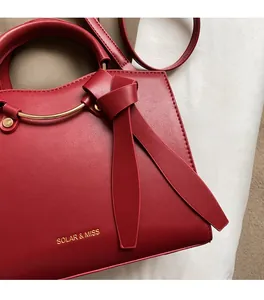 Gros plan du sac cabas bordeaux avec logo doré et détail de poignée ronde en métal