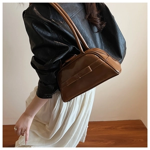 Brown glossy patent leather Boston bag with bow detail worn by a model in casual style