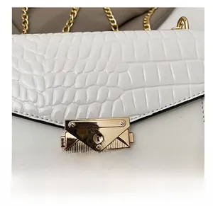 Detailed macro view of gold metal buckle and crocodile texture on white crossbody bag