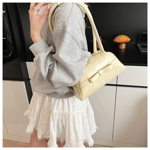 Side view of cream beige bow shoulder bag on a female model in a modern kitchen