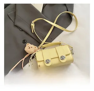 Detail of pale yellow crocodile texture leather bag with silver buckles and bear charm