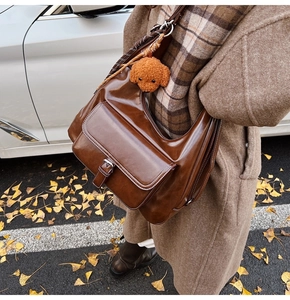 Detail view of large dark brown leather crossbody bag with silver buckle and plush dog charm