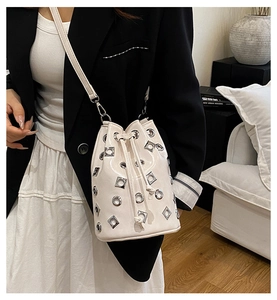 Detail of cream bucket bag with silver grommets and adjustable shoulder strap worn by model