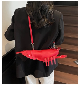 Detail of red lobster-shaped crossbody bag with gold rivets worn by a model