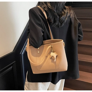 Detailed view of beige tote bag with litchi grain texture and elephant charm accessory