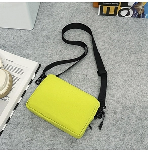 Detail of neon green nylon crossbody bag with black adjustable strap and double zippers