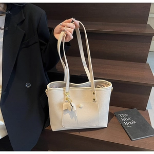 Detailed macro view of the cream tote bag showing its pebbled leather texture and bow detail