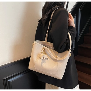 Detail of beige lychee grain leather tote bag with a cute elephant charm accessory
