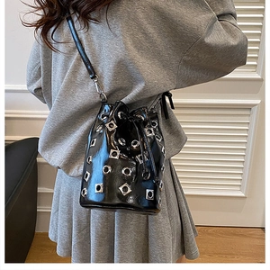 Detail of black glossy bucket bag with silver metal eyelets and drawstring closure