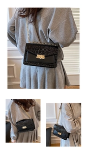 Detail of black faux crocodile leather crossbody bag with gold chain and metal buckle