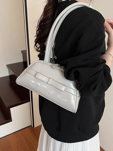 Glossy light gray handbag with bow decoration worn as an elegant underarm shoulder bag