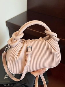 Pink pleated crossbody handbag with circular handle and silver hardware in lifestyle setting