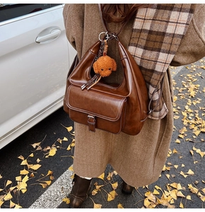 Close-up of brown oil-wax leather shoulder bag with white stitching and teddy bear charm