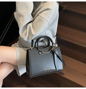 Détail d'un sac à main noir en cuir avec nœud en soie et poignée ronde en métal doré