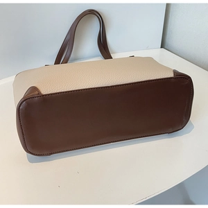 Dettaglio del fondo largo e delle cuciture in pelle marrone su borsa tote crema