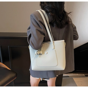 Detail of grey lychee leather tote bag with exterior pocket and bow charm on model