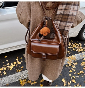 Detail of vintage brown oil wax leather shoulder bag with white stitching and dog charm