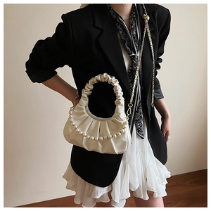 Detail of beige pleated croissant bag with pearl chain strap worn with black blazer