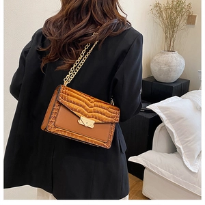 Close-up of brown crocodile texture flap bag with a thick gold chain strap on a model