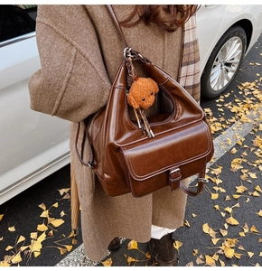 Detail of vintage brown oil wax leather shoulder bag with plush dog charm in autumn setting
