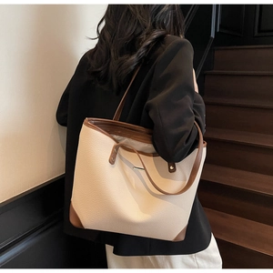 Borsa tote crema con bordo marrone e dettaglio in metallo in un contesto formale