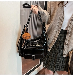 Detail of black oil wax leather shoulder bag with white stitching and bear charm