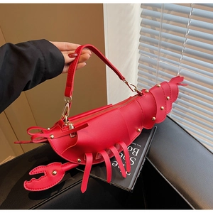 Detailed view of red lobster shaped crossbody bag with gold rivets on a book