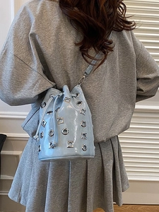 Light blue metallic bucket bag with silver grommets worn by a model in casual outfit