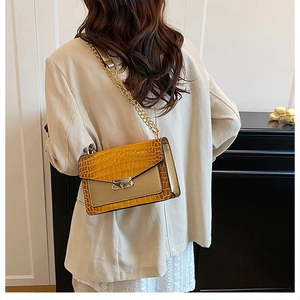 Detail showing the crocodile pattern texture and metal chain strap on the yellow flap bag