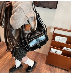 Detail of black glossy crescent bag with leather buckle and brown teddy bear charm