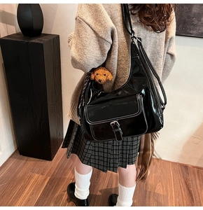 Detail of black glossy faux leather shoulder bag with white stitching and puppy charm