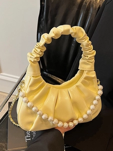 Pale yellow pleated cloud handbag with elegant pearl strap on a black leather chair