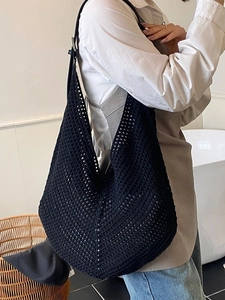 Large black woven crochet tote bag with adjustable leather shoulder strap on model