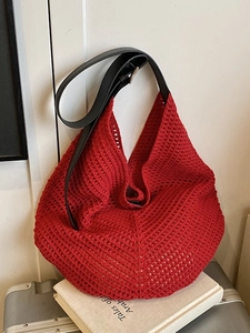 Large red hand-woven tote bag with black leather strap on a travel suitcase