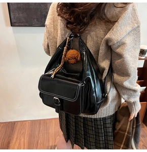 Glossy black oil wax leather backpack with contrast stitching and a teddy bear charm