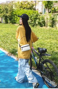 Outdoor view of a white nylon crossbody bag with black zipper on a female model