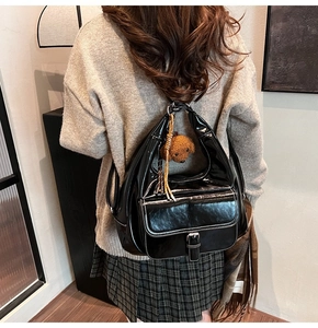 Detail of black glossy shoulder bag with white stitching and plush bear charm on model