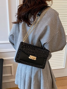 Vintage black crocodile texture crossbody bag with gold chain strap on grey dress model