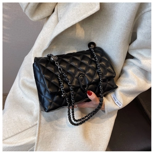 Detail of black quilted leather crossbody bag with dark metal chain and stitch texture