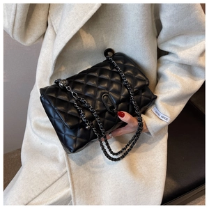 Detail view of black quilted chain bag with metal clasp and leather woven shoulder strap